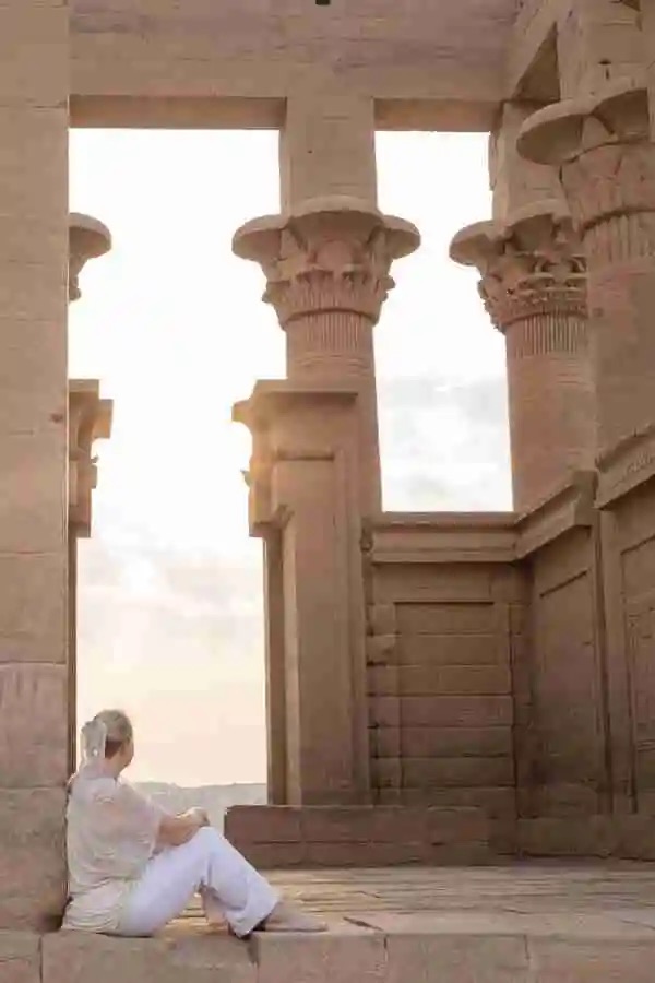 A woman in white sitting on the steps of an ancient Egyptian temple at sunrise