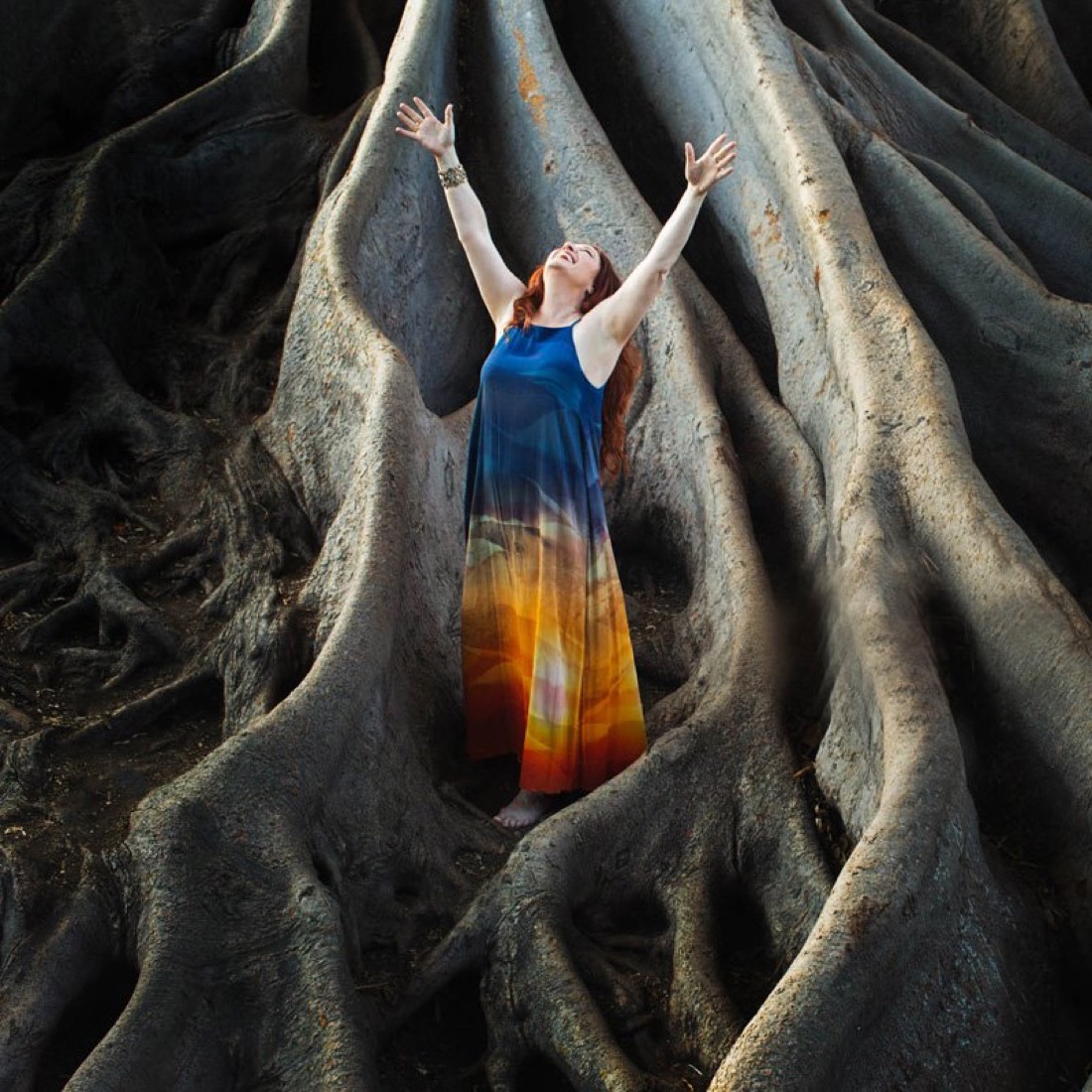 Halle standing with her arms raised inside the giant roots of an ancient tree