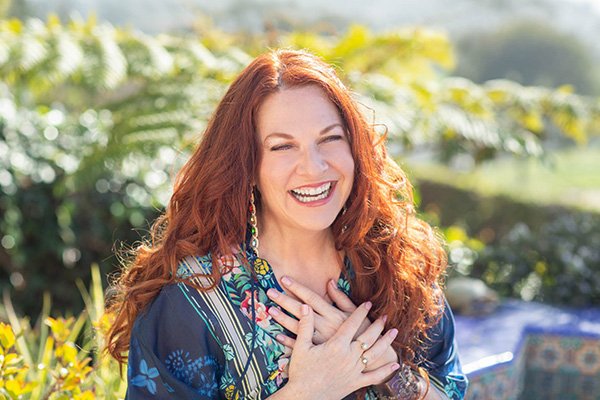 Halle Eavelyn laughing with both hands on her heart, in a blue floral kimono in a sunlit garden