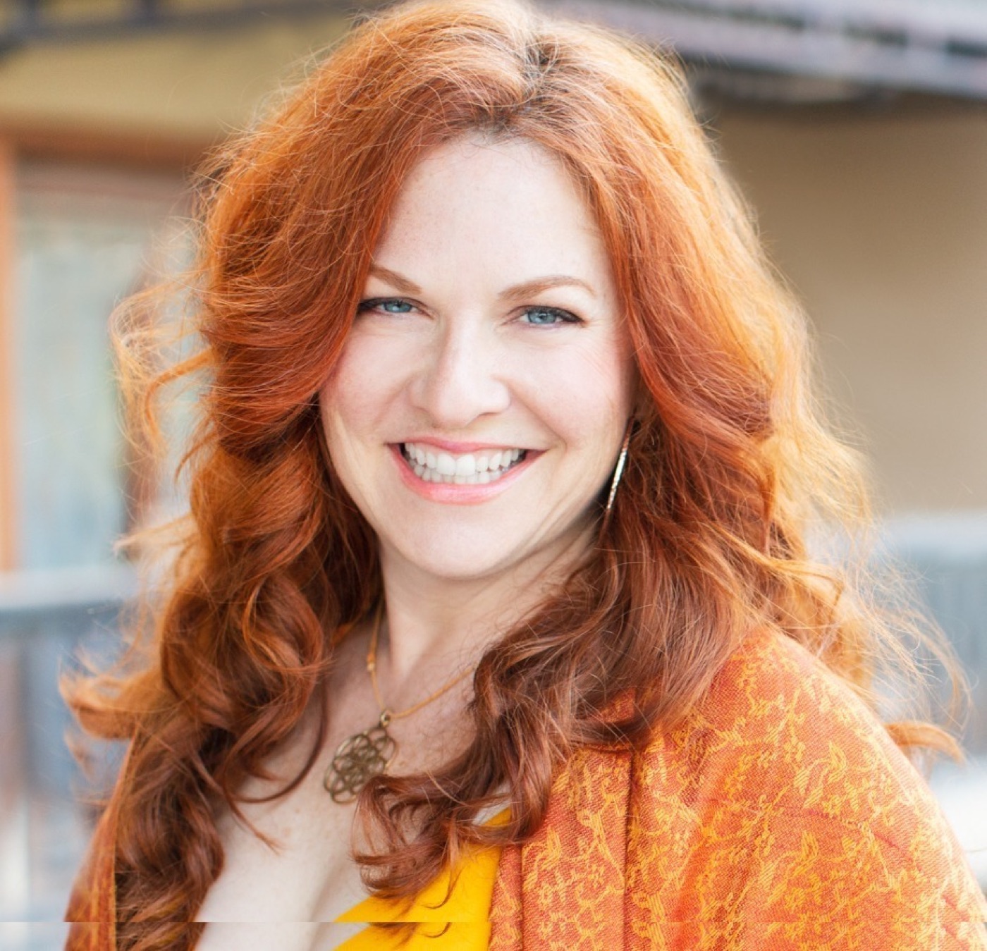 Halle Eavelyn print headshot, smiling, red hair, orange lace jacket over a yellow top